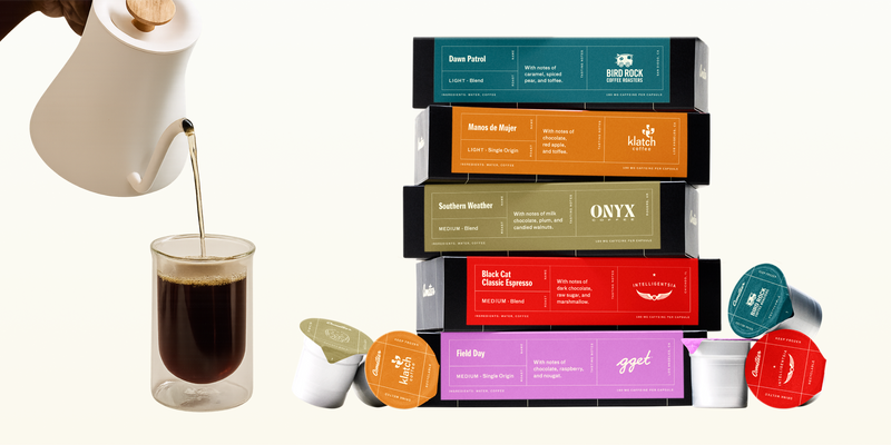 Stacked boxes of assorted light, medium, and dark roast coffee capsules with a white kettle pouring coffee into a glass cup