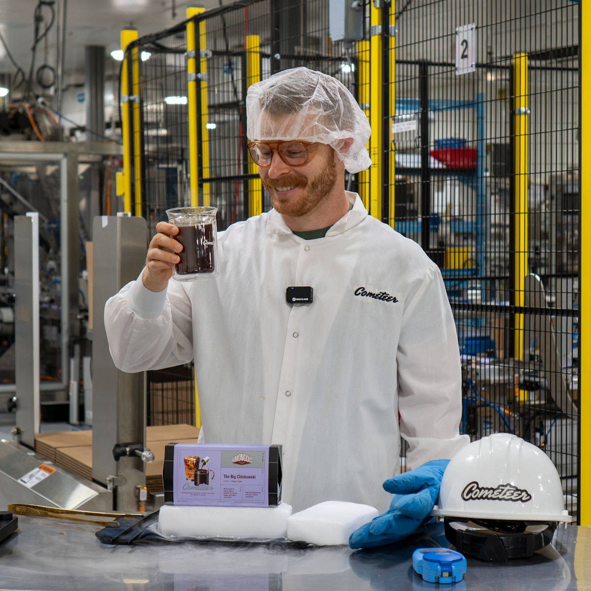 Ethan Chlebowski holding a glass of black coffee at the Cometeer factory.