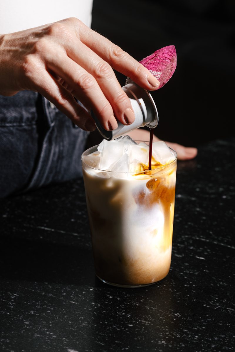 Pouring concentrated Cometeer coffee from an opened capsule into iced milk