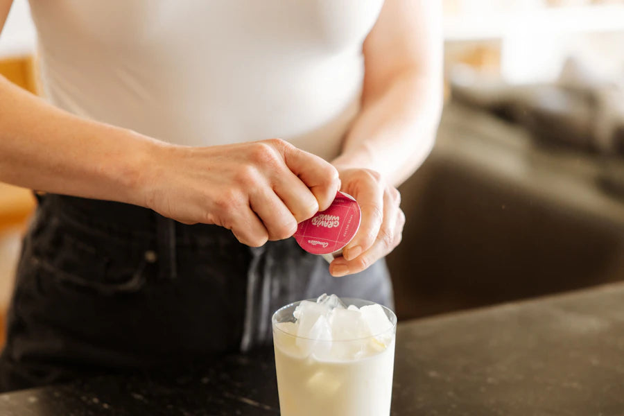 Hands opening a Cometeer capsule above a glass of iced milk
