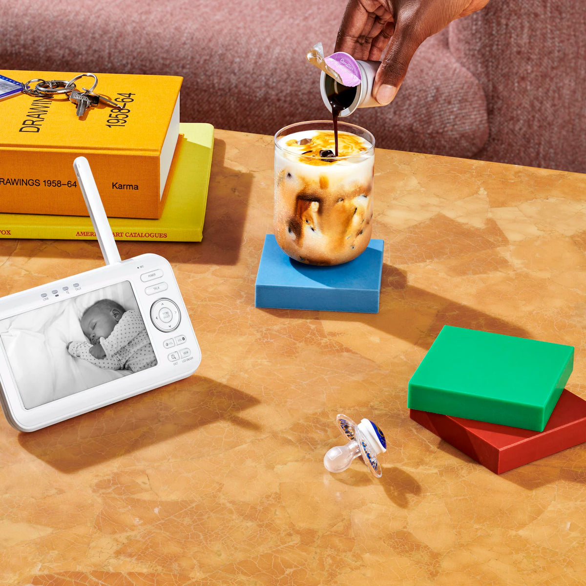 Coffee being poured from a Cometeer capsule into an iced latte beside a baby monitor.