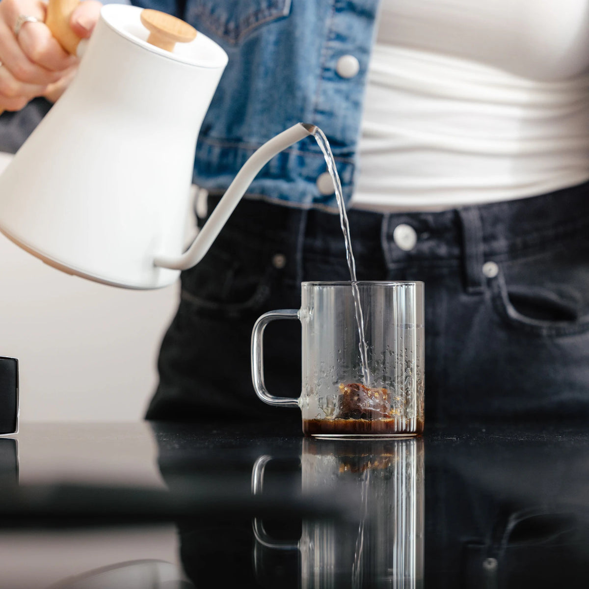 Hot water being poured over frozen coffee in a clear mug.