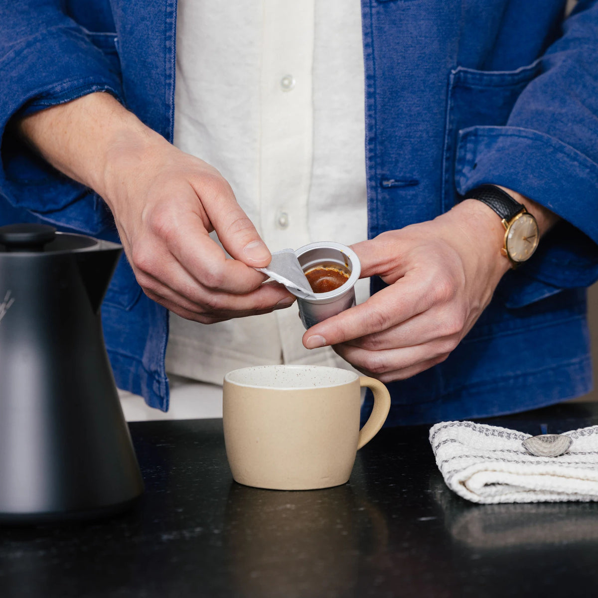 Hands peeling the lid from a Cometeer capsule above a mug.